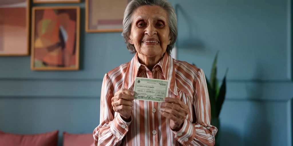 Eleitora idosa sorri segurando o título de eleitor